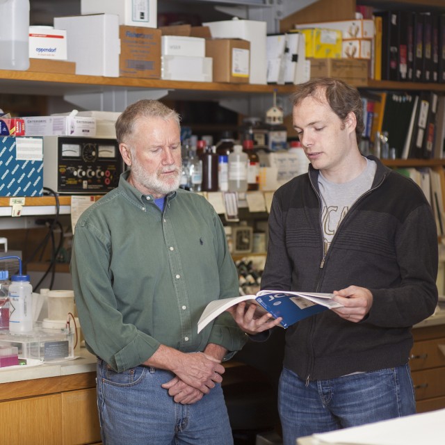 two researchers standing in lab reading a book 